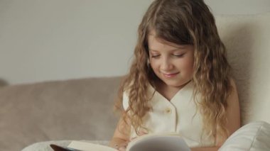 Kıvırcık saçlı genç bir kız rahatça oturur ve kitap okur. Sayfaları çevirir ve içeriğe gülümser..