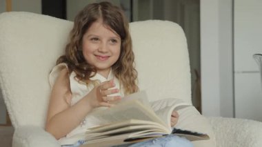Genç bir kız kendini kitaplara kaptırmış beyaz bir sandalyede rahatça oturuyor. Sayfaları çevirirken gülümsüyor, belli ki okuma zamanından zevk alıyor..
