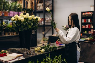 Çiçekçi tezgahta taze bir buket beyaz gül düzenliyor. Küçük bir işletme ortamında elle çiçek tasarımı yapıyor.