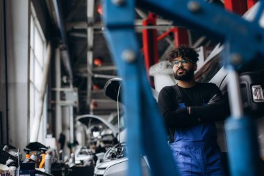 Genç bir erkek otomotiv teknisyeni modern bir araba tamirhanesinde çalışıyor.