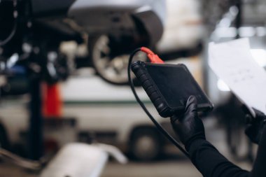 Eldivenlerde otomatik tamirci elleri kağıt ile tarama tarayıcısı tutuyor, servis istasyonunda tamir için araç sistemini kontrol ediyor.