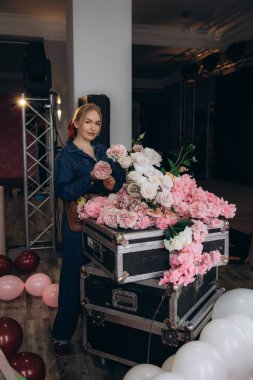 Yol kenarlarında pembe ve beyaz çiçekler düzenleyen etkinlik planlayıcısı, balonlarla ve sahne ışıklarıyla bir kutlamaya hazırlanıyor