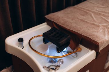 Saç yıkama lavabosu, ayarlanabilir başlık ve su akışıyla modern bir güzellik salonunda bir sandalyenin yanına yerleştirilmiş.