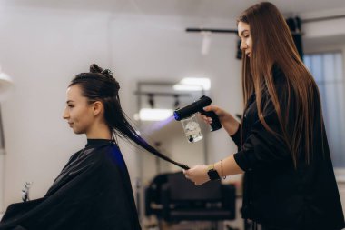 Güzellik salonunda ileri derecede nemlendirici ve canlandırıcı tedaviler için bir kadının saçına nano sprey tabanca kullanan kuaför.