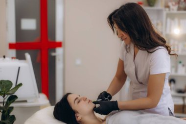Modern bir güzellik kliniğinde estetik gelişim için kadının dudaklarına hyaluronik asit enjekte eden profesyonel kozmetikçi.