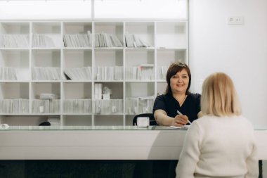 Dostane yönetici, bir sağlık kliniğinin resepsiyonunda bir hastaya evrak işlerinde yardım ediyor, tıbbi kayıtları yönetiyor.