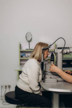 Üst düzey kadın, modern bir klinikteki bir optometristin ileri düzey tıbbi ekipmanlarıyla kapsamlı bir vizyon muayenesi alıyor.