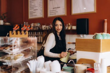 Gülümseyen kadın barista modern bir kafede taze kahve hazırlıyor, konukseverlik hizmeti veriyor.