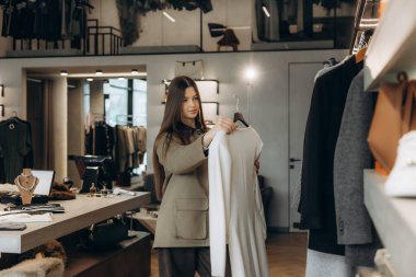 Modern bir perakende mağazasında askılardan şık kıyafetler seçen genç bir kadın. Yeni kıyafetler satın alınıyor