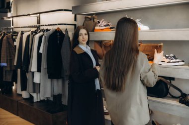 Perakende terapiden hoşlanan iki genç kadın, modern moda mağazasında kıyafet ve aksesuarlara göz atıyorlar.