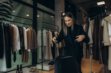 Siyah alışveriş torbaları tutan genç bir kadın, modern bir giyim mağazasında başarılı bir perakende satış deneyimi yaşıyor.