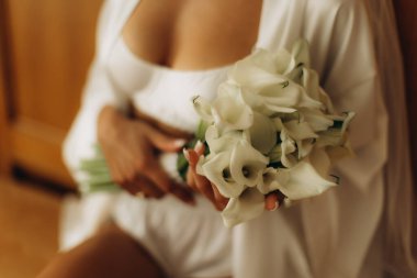 Beyaz bir elbise ve iç çamaşırı giyerken beyaz bir zambak buketi tutan zarif kadın özel bir güne hazırlanıyor.