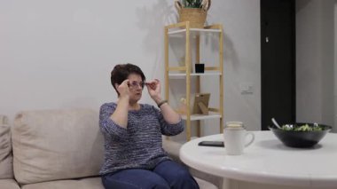 Yaşlı bir kadın evde vakit geçirmekten zevk alıyor, televizyon izlemekle cep telefonunu kullanmak arasında gidip geliyor.