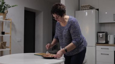 Kıdemli kadın tabak üzerinde kıyma sosu hazırlıyor. Çağdaş mutfağın içinde ev yapımı yemek hazırlarken malzemeleri dikkatlice karıştırıyor.