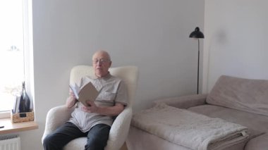 Kafkasyalı, gözlüklü, rahat bir koltukta oturup kitap okuyan yaşlı bir adam. Huzurlu yaşlı vatandaş emekliliğinin tadını çıkarıyor