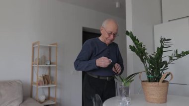 Gözlüklü yaşlı adam yeşil bir bitkinin yapraklarından tozu dikkatle siliyor. Hobi olarak evde bahçıvanlık ve bitki bakımı