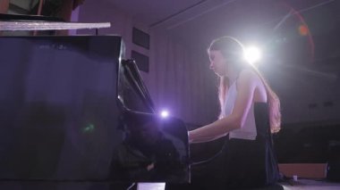 Sahnede sahne ışıkları olan bir piyanoda klasik müzik parçası çalan genç bir piyanist.