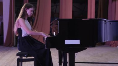 Profesyonel bayan piyanist loş bir sahnede klasik müzik çalıyor zarif hareketler ve yoğun sanatsal tutku ile büyük bir piyano çalıyor.