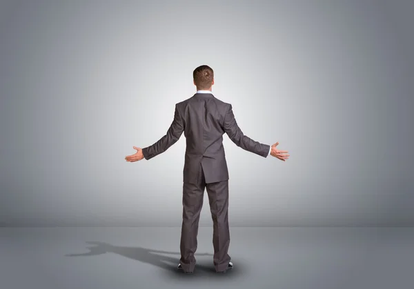 Businessman standing in an empty gray room. Rear view