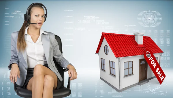 Businesswoman in headset, model house with tag for sale beside