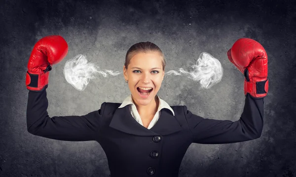 Businesswoman in boxing gloves posing with her arms up, shouting, smoke from ears