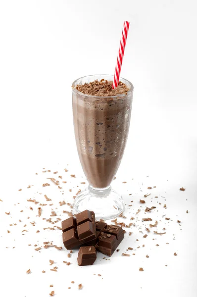 Chocolate ice cream milkshake drink in a vintage glass with a striped straw with whole chocolate and grinded pieces around isolated on white background