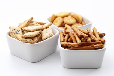 Beyaz arka planda izole edilmiş seramik kaselerde kraker, kraker ve tuzlu atıştırmalık seçimi