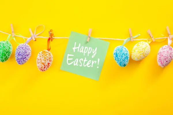 Christianity, Christian tradition concept with colorful Easter Eggs painted in various colors and decorated with white beads hanging on a string or rope next to a paper that reads Happy Easter!