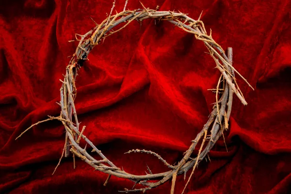 Easter holidays, christian celebration of Jesus resurrection and the Passion of Christ concept with frame made by a crown of thorns on red velvet with dramatic light and copy space