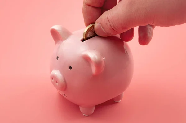Prosperity in personal finances, money growth, modern economics and saving capital conceptual theme with hand investing for retirement by putting a coin in the piggy bank isolated on pink background