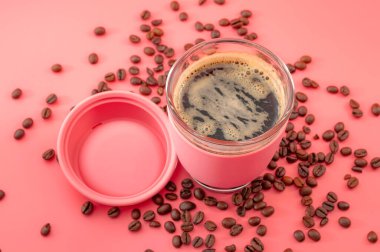 Kahve molası, kafein ve enerji bir fincan kahve konsepti temalı yeniden kullanılabilir cam bardak sıcak içecek bardağı pembe arka planda izole edilmiş taze fasulyelerle çevrili.