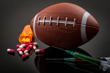 Amerikan futbolu ile spor ve steroid bağımlılığı konsepti, bir şişe reçeteli hap ve siyah arka planda yeşil ve kırmızı sıvılı şırınga.