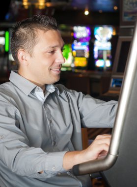 Yaşlarının saç jölesi ve gri gömlek giyen genç adam bir slot makinesidir oynuyor