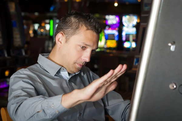 Giovane uomo sulla ventina indossa gel per capelli e una camicia grigia sta giocando una slot machine — Foto Stock