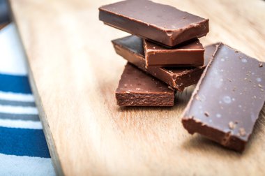 Chocolate pieces stacked on a wooden table and a kitchen table