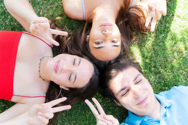 Groupe d'amis adolescents heureux se détendre sur l'herbe verte dans la prairie et montrant signe de paix — Photo