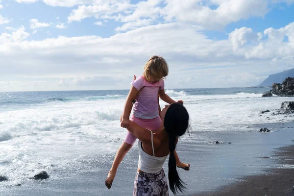 Happy little girl daughter enjoying vacation with mother while standing on beach — Stock Photo, Image