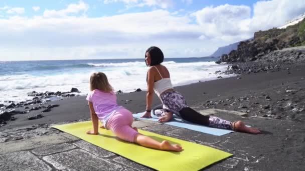 Gesunde glückliche Familienmutter und Tochter machen Dehnübungen am Meer — Stockvideo