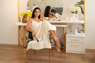 İpek elbiseli, gülümseyen esmer kadın kameraya bakıyor.