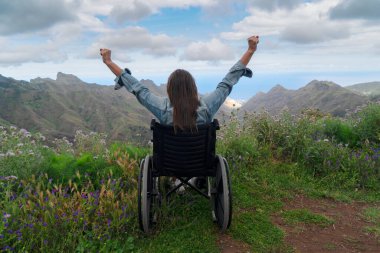 Disabled handicapped woman in wheelchair on mountain hill enjoying view clipart