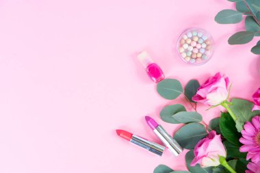 Çiçekleri ve kozmetik ürünleri olan pembe düz yatak örtüsü, yumuşak kadın havası, gül buketi ve okaliptüs dalları ruj, pudra, boncuklu mücevher ve pastelin yanında düzenlenmiş.