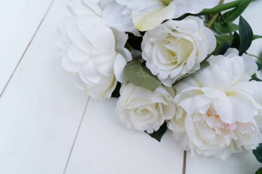 Beyaz çiçekler beyaz ahşap arka planda, narin kamelya gülleri parlak yeşil yapraklarla sade gelinlik tasarımı için düzenlenmiş, yumuşak doğal ışık, yatay