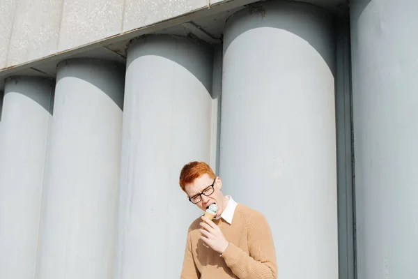안경을 쓴 굶주린 젊은 생강 남자가 아이스크림 콘을 먹고 있다 — 스톡 사진