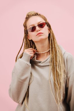 Dar güneş gözlüklü, hoş görünümlü, pembe arka planda sarı örgü saçları olan genç bir kadın. Başını dik tut, kibirli surat. İnci kolye tutuyordu.