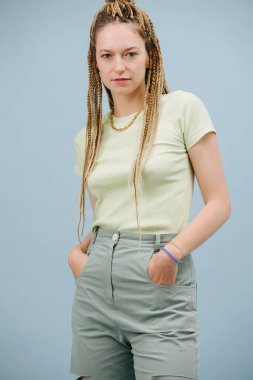 Mavi arka planda şık sarı örgü ören genç bir kadın. Kameraya bakıyorum, eller cepte..