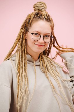 Yuvarlak gözlüklü, güzel, gülümseyen bir kadın. Pembe arka planda zarif, sarı saç örgüleri olan. Sevimli oynuyor, elinde saç tutuyor..