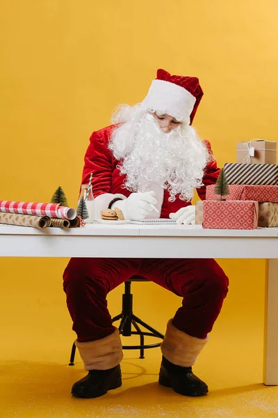 Santa Claus Píše Dopis Stolu Žlutém Pozadí Kvalitní Fotografie — Stock fotografie
