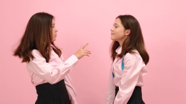 Schöne kleine Zwillingsschülerinnen, die Spaß am Kämpfen mit ihren Rucksäcken haben. Über rosa Hintergrund Studio-Video.