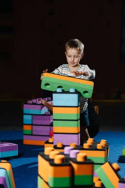 Dalgın çocuk eğlence merkezinde büyük yumuşak inşaat parçalarıyla oynuyor.