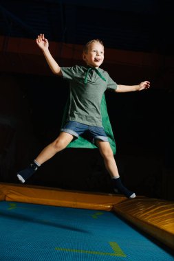 Eğlence merkezinde trambolinde zıplayan pelerinli kendinden emin bir çocuk.